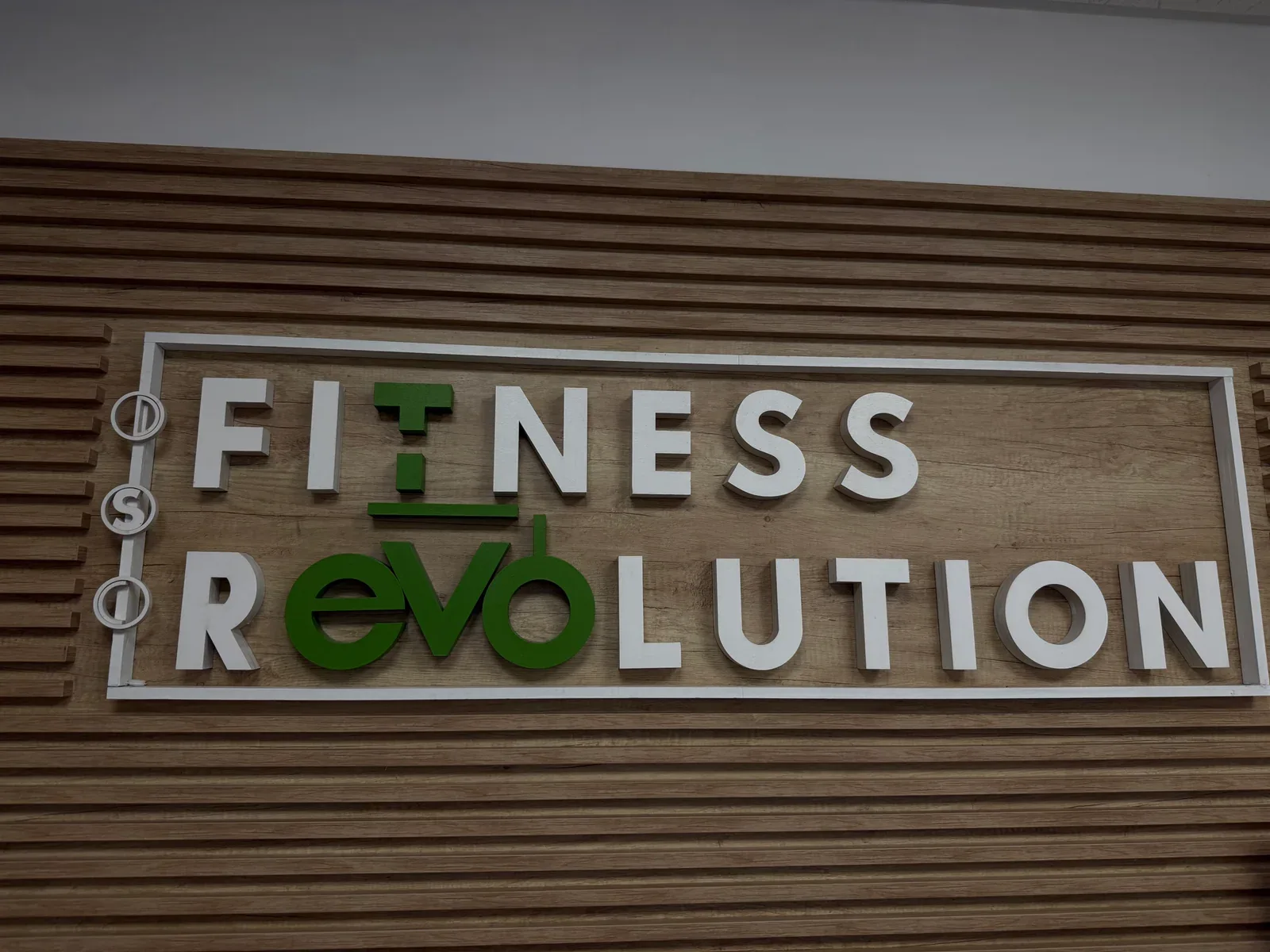 Sigla DSC Fitness Revolution, cu litere albe și verzi pe peretele din lemn